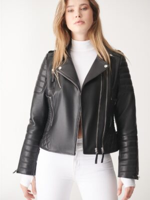 Front close-up of a woman in a black leather biker jacket with silver zippers, white turtleneck, and sleek silhouette.
